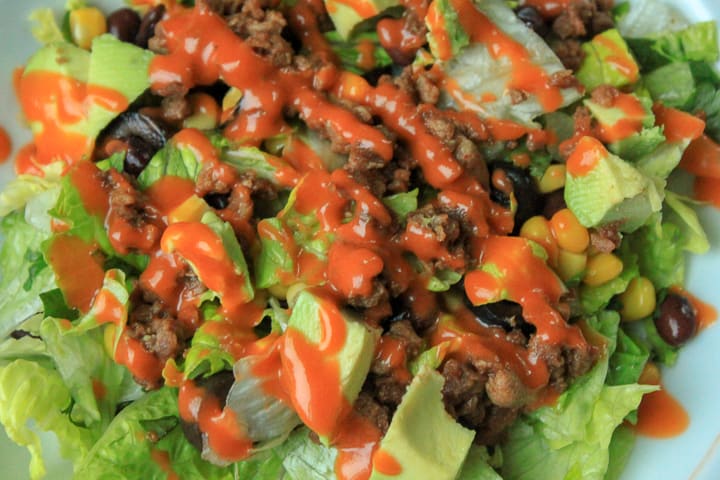 vegan taco salad toppings with dressing on a bed of lettuce up close photo. 