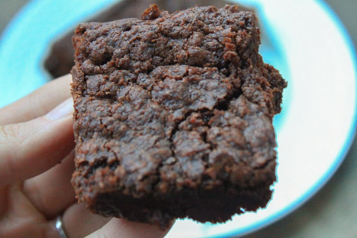 vegan brownie in a hand with a white plate in the background. 