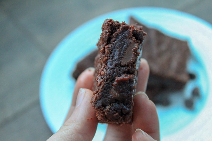 vegan brownie held in a hand with the background blurred of a white plate with more brownies. 