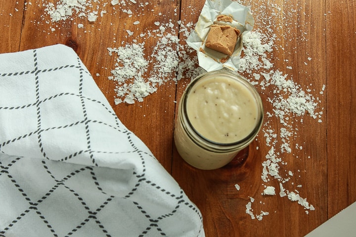 vegan cream of potato soup in a mason jar on a wood background with potato flakes sprinkled. 