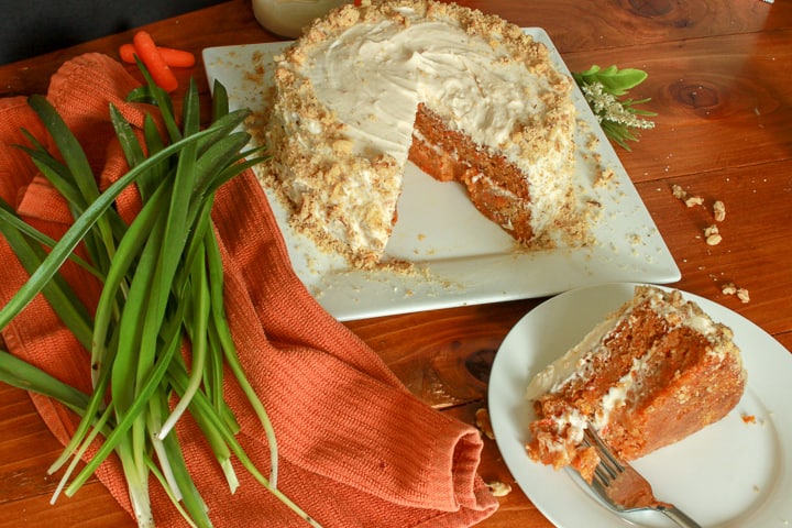 vegan carrot cake with a slice out of it on wood table. 