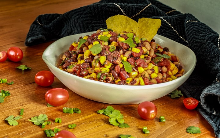 cowboy caviar in a bowl on wood with chips in it and tomatoes/cilantro around it. 