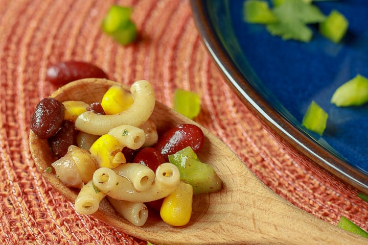 Mexican Pasta Salad on a wooden spoon on a orange background. 