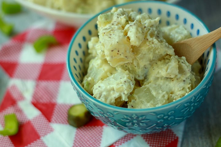 Vegan Potato Salad in a blue blue with a wooden soon and a white and red checkered background. 