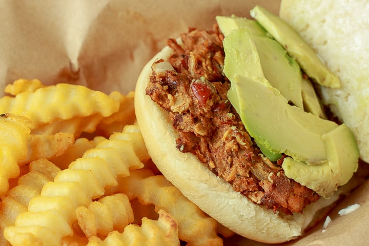 Vegan BBQ bean Burger open faced with avocado on it laying on a bed of fries.