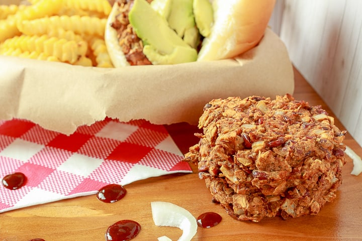 Vegan bbq bean burger patties stacked 3 high with a made burger and fries in the background. 