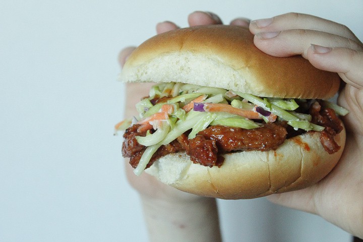 vegan pulled pork sandwich with coleslaw held in someones hand with a white background. 