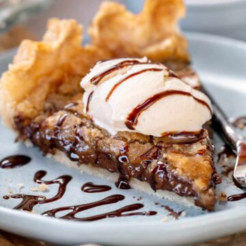 A single slice of a vegan chocolate chip pie with ice cream and chocolate sauce drizzle.