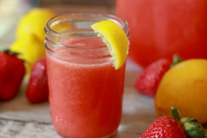 strawberry lemonade in a cup with a lemon slice on the edge and lemon and strawberries around it. 