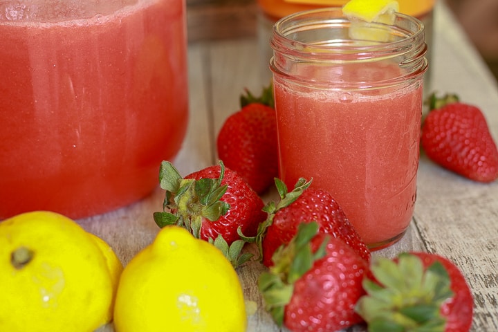fresh strawberry lemonade in a small glass cup with strawberries and lemon around it. 