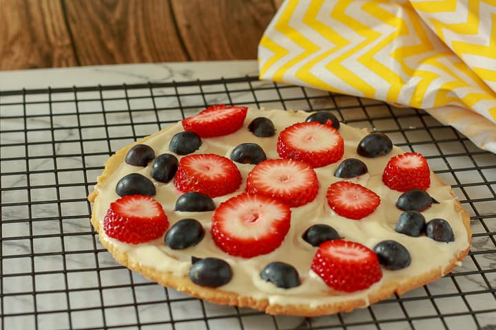 Large Vegan fruit pizza on a cooling rack decorated with fruit, 
