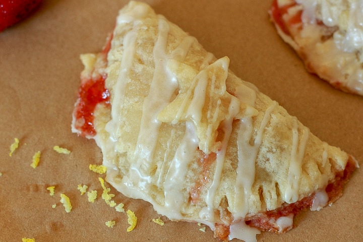 one vegan hand pie with a pie crust start on it drizzled with glaze and some lemon zest on a brown background. 