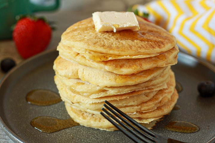 vegan pancake stack with a vegan butter dollop on top and syrup on a black black. 