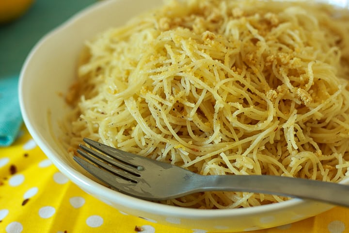 vegan lemon pasta in a white bowl with a fork on a yellow polka dot background. 