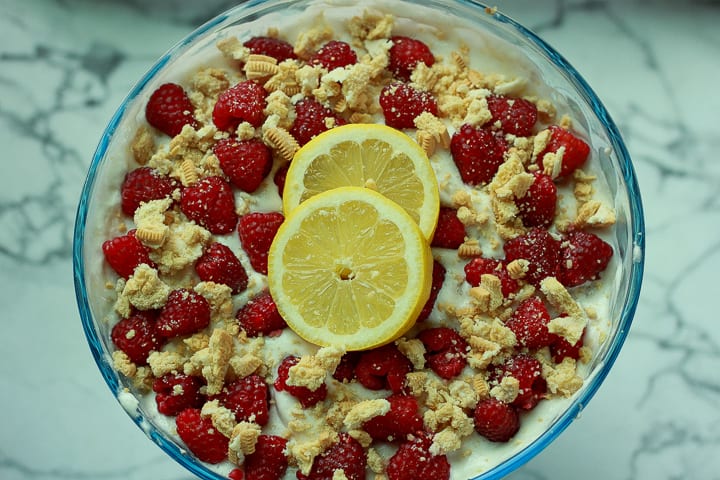vegan raspberry lemon trifle in a large bowl with two lemons on it on a marble background. 