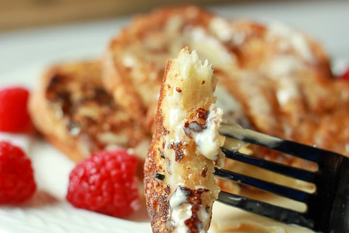 vegan french toast bite  on a black fork with french toast and raspberries in the background. 