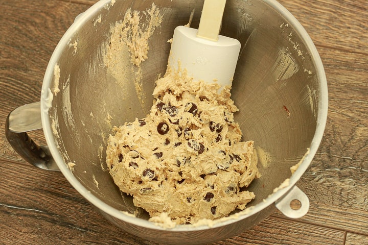 vegan chocolate chip cookie dough in a metal bowl with a white spatula on a wood background. 