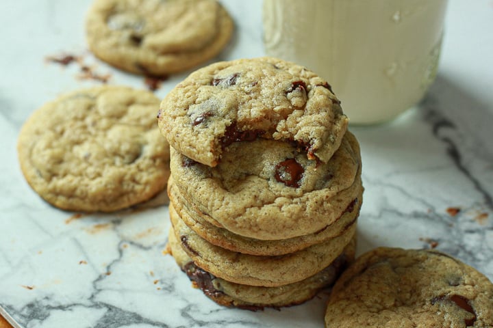 Classic Vegan Chocolate Chip Cookies stacked with a bite out of the top one on a marble background. 
