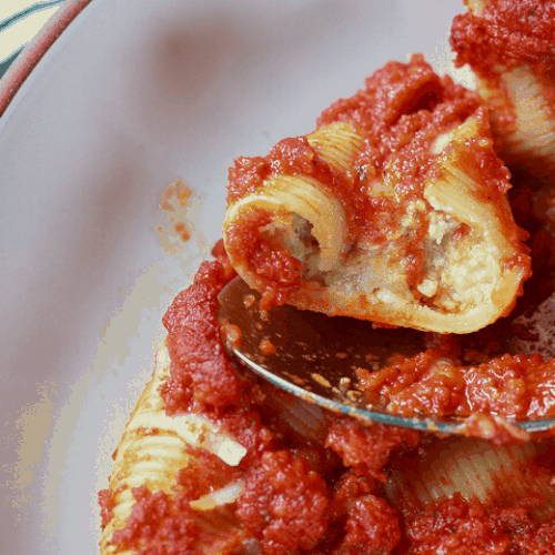 vegan ricotta stuffed shells piled together on a white background with a spoon holding up a half cut shell. 