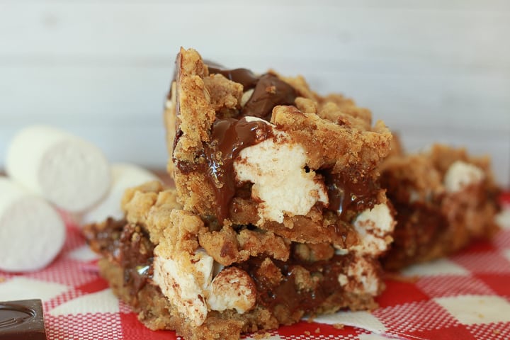 vegan smores bars on top of each other with marshmallows in the back and red and white checkered napkin. 