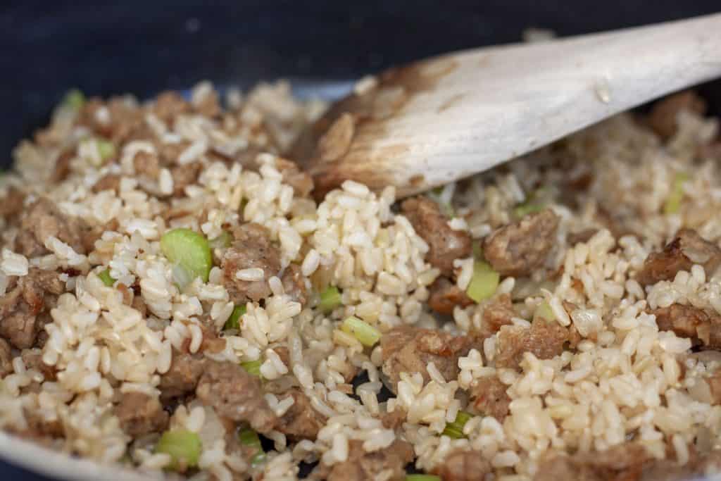 rice, vegan sausage, vegetables mixed cooking in a skillet with  wooden spoon. 