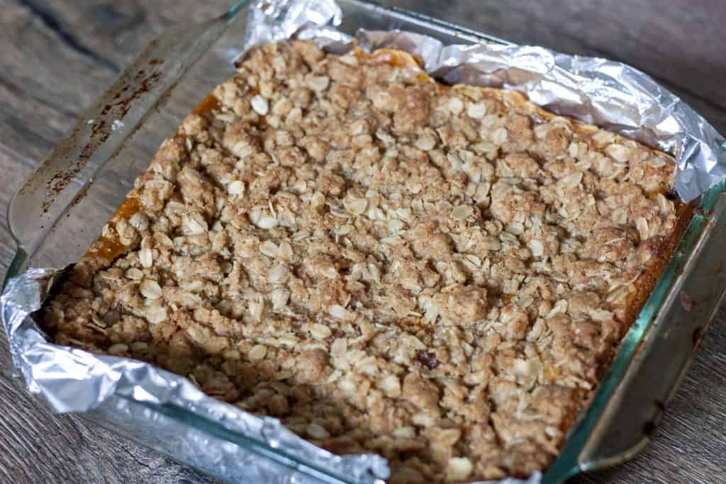 cooked pumpkin pie bars in glass 8x8 pan with foil hanging out the sides.