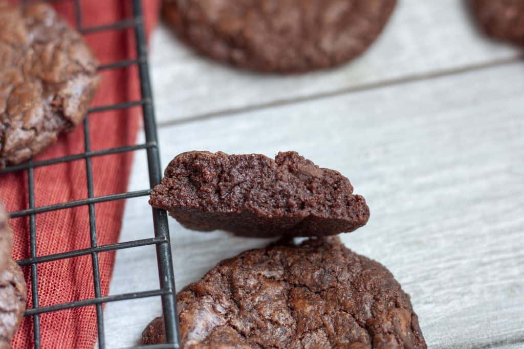 thick vegan brownie cookies on a white wood background with a half cut cookie so you can see the inside. 