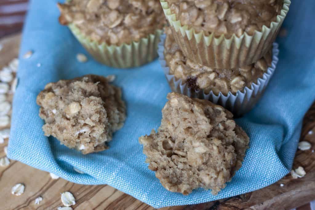 Vegan Oatmeal Muffins stacked and one open on a blue background. 