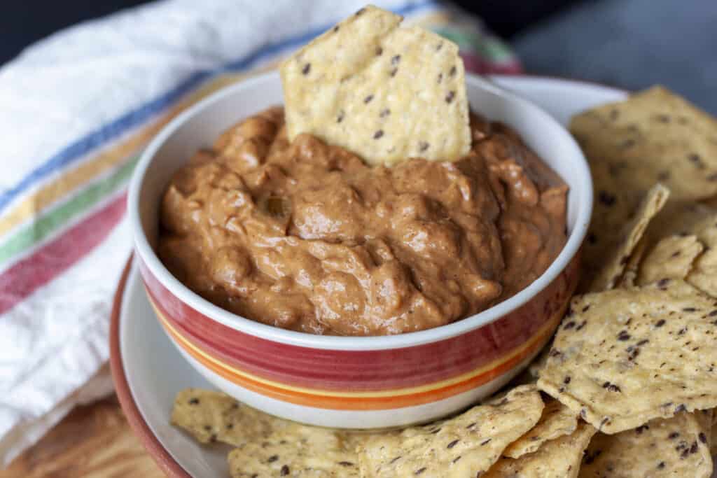 vegan bean dip in a bowl with chips around it and one chip dipped into the dip. 