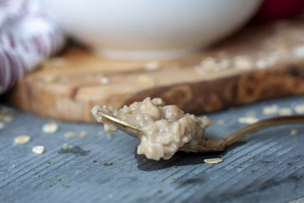 vegan apple cinnamon oatmeal on a gold spoon on a grey background.