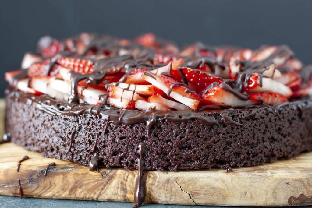 A whole vegan chocolate strawberry cake on a wood platter.