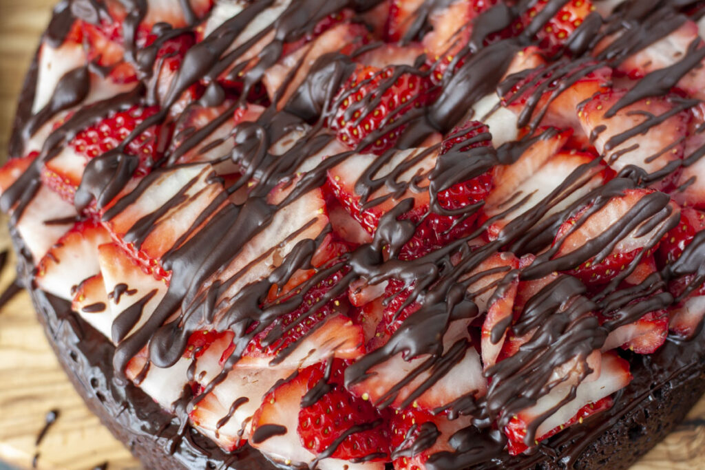 Vegan chocolate covered cake decorated with the strawberries and chocolate ribbons.