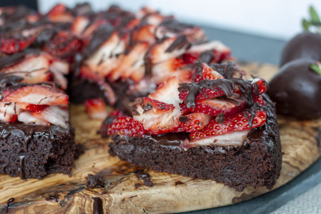 slice of vegan chocolate covered strawberry cake on a wood background.