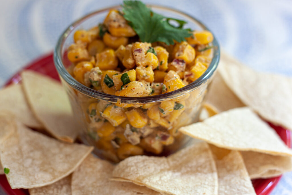 vegan elote dip ni a small glass bowl with chips around it. 