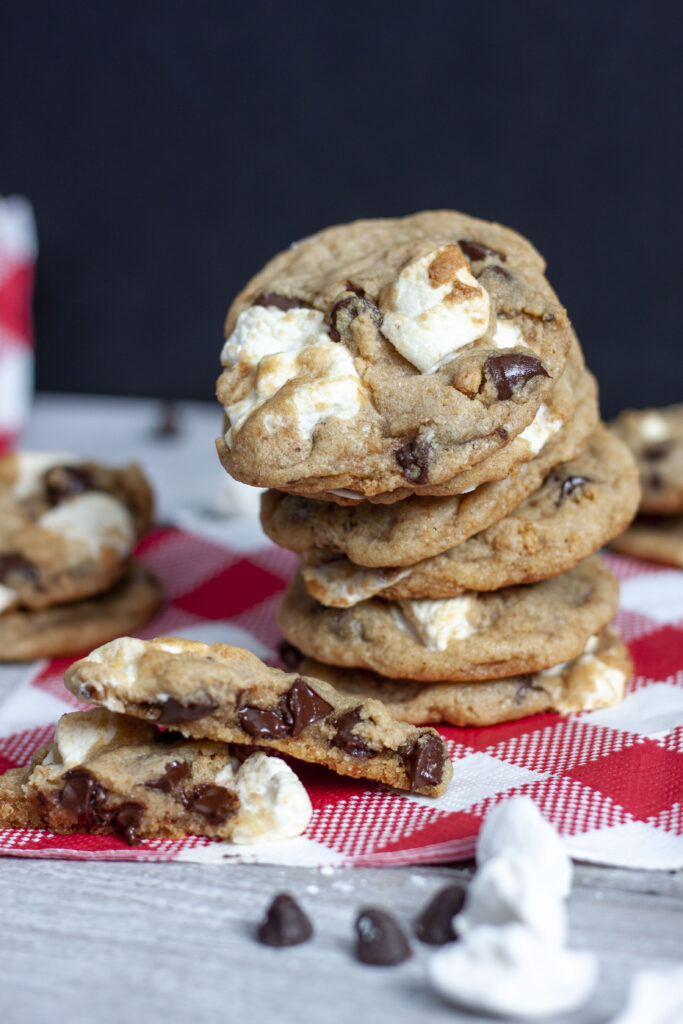 Vegan s'mores cookie leaning stack with a cut cookie at the bottom on a checkered white and red napkin. 