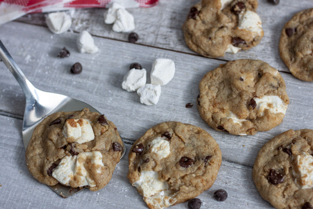 vegan s'mores cookies on white wood with a cookie on a spatula. 