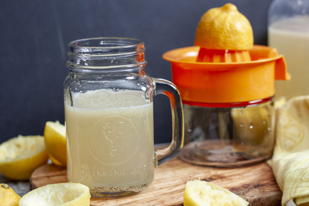 classic lemonade in a cup with a handle  with a lemon juicer next to it and lemons around it. 