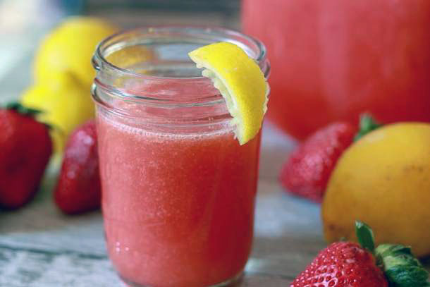 strawberry lemonade in a small cup with a lemon wedge and lemon and strawberries around it. 