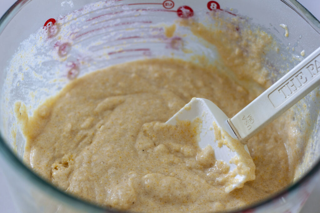 the cornbread batter in a glass bowl with a spatula. 