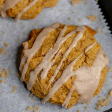 Single vegan pumpkin cookie on a white background with some cookie crumbs around it and a cinnamon drizzle on the cookie.