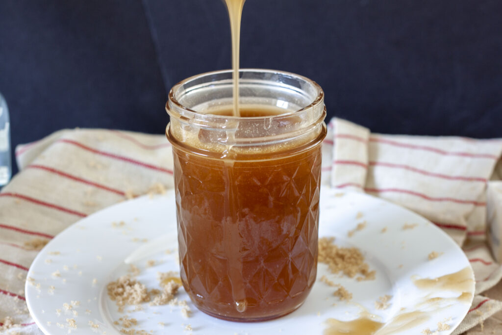 vegan caramel sauce with almond milk in a glass mason jar on a white plate with a drizzle of caramel. 