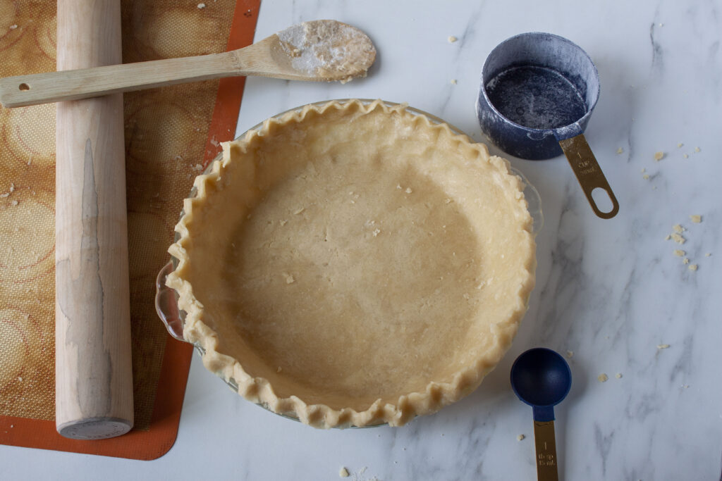 vegan pie crust in a pie plate with a wooden spoon, 1 cup measuring cup, 1 tb and a rolling pin.