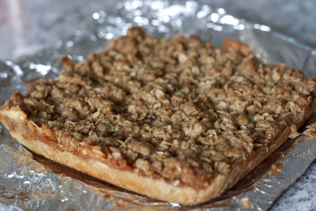 vegan apple pie bars out of the 8x8 pan in a full square on a foil background.