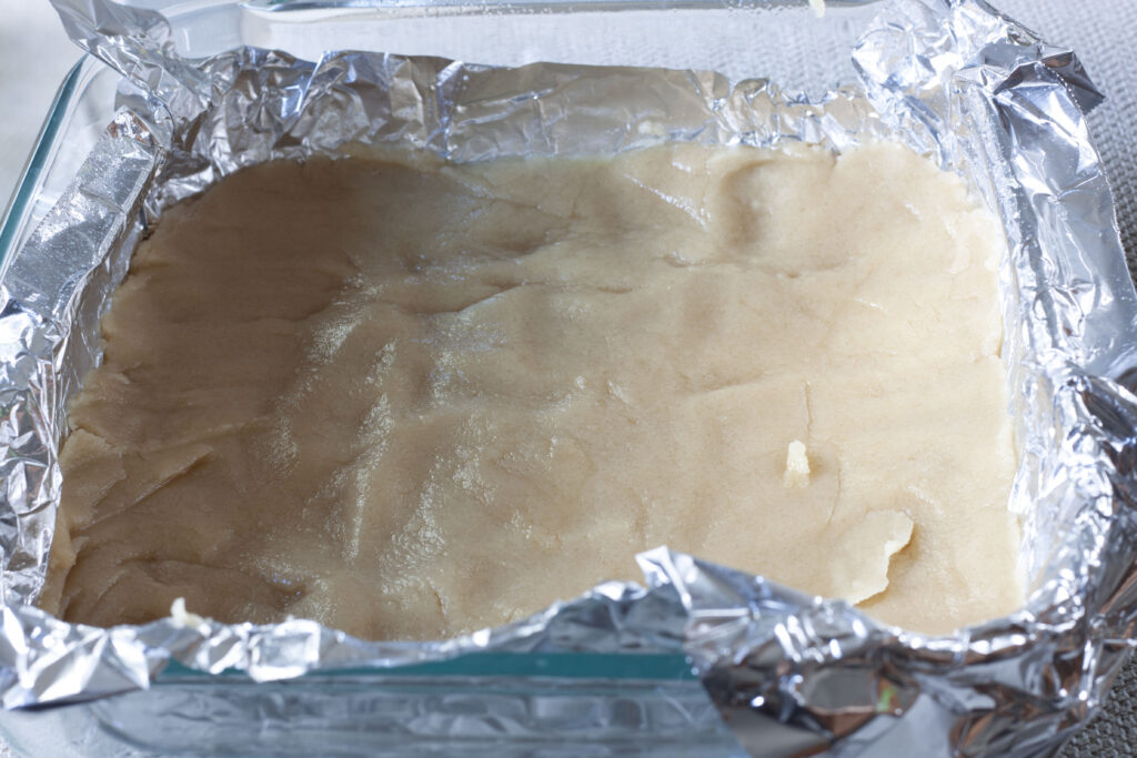 vegan shortbread apple pie crust rolled out into a 8x8 pan that has foil on it.
