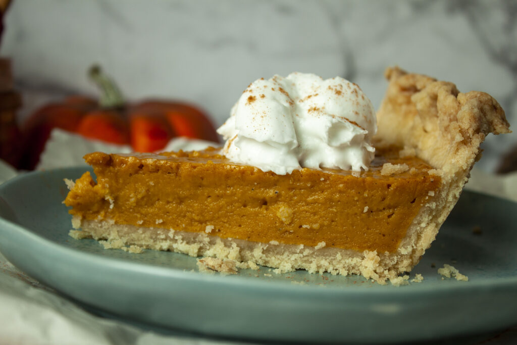 slice of vegan pumpkin pie with whipped topping on a blue plate.