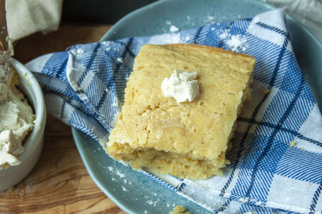 vegan cornbread with butter on top on a plate with a blue and white checkered napkin. 