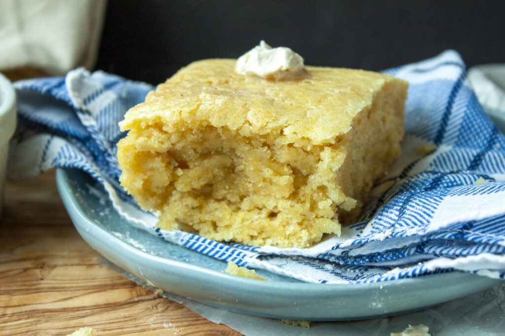 vegan cornbread with butter on top on a plate with a blue and white checkered napkin. 