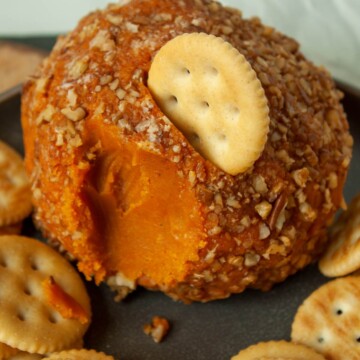 An upclose shot of a vegan cheese ball with a bite out of it and a cracker in the middle.