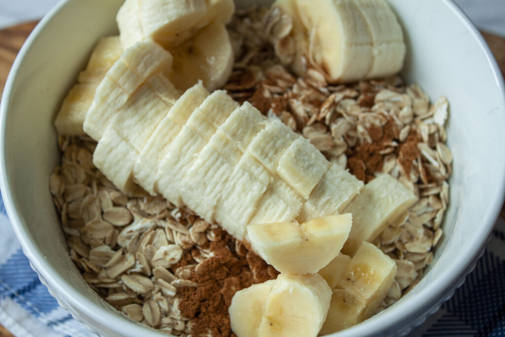 vegan overnight oats before the plant milk with chunks of banana and visible cinnamon in a white bowl. 