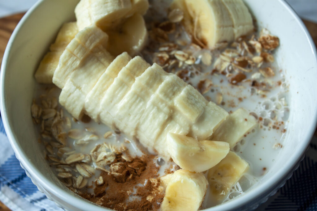 vegan oats before stirring with oats, non dairy milk, chunks of banana, and visible cinnamon in a white bowl. 